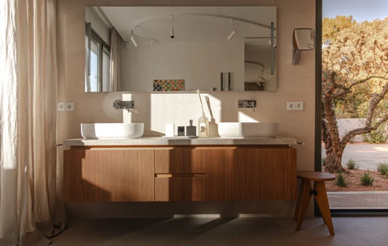 Mueble de baño de madera ranurada con dos lavabos sobre encimera de terrazo y espejo en el proyecto Pinar de Sa Dutxeta