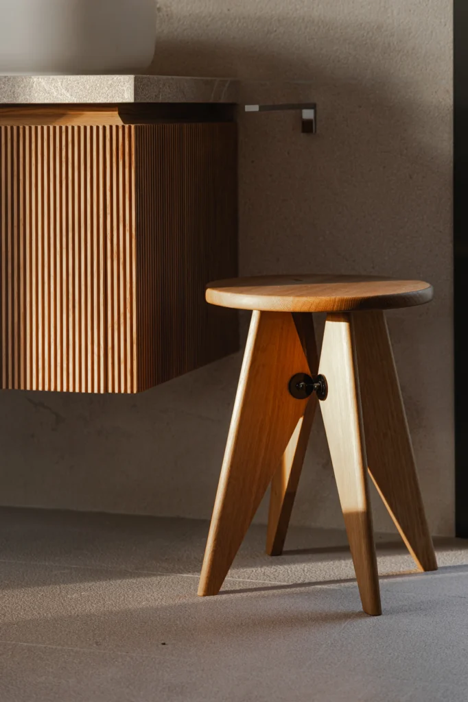 Taburete de madera junto al mueble ranurado del baño en el proyecto Pinar de Sa Dutxeta