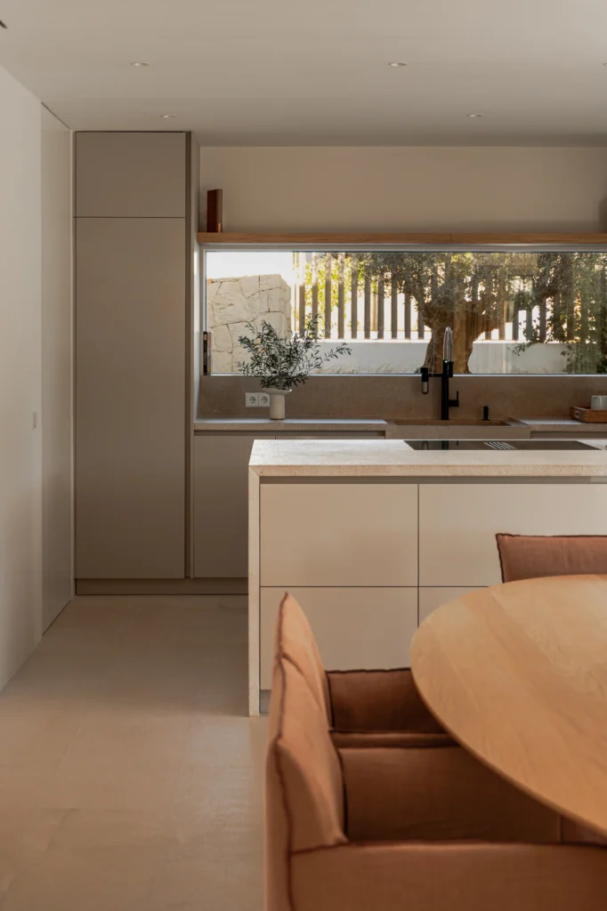 Cocina con despensa integrada y ventana alargada sobre la encimera en el proyecto Pinar de Sa Dutxeta