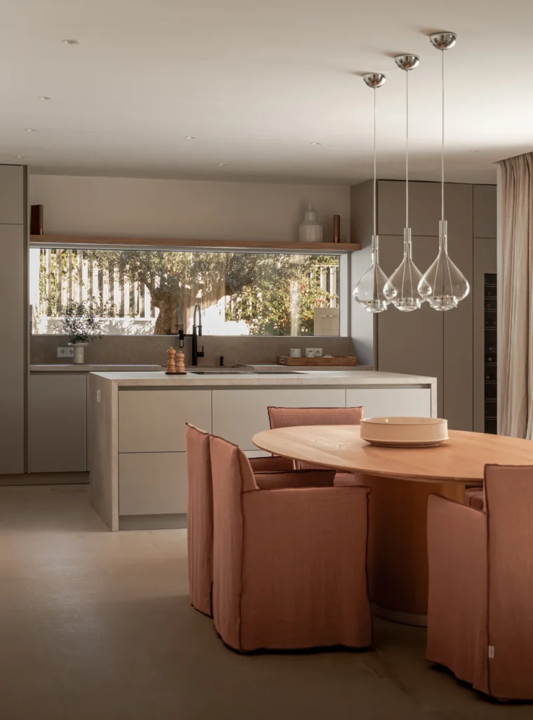 Comedor junto a la cocina con lámparas y mesa de terracota en el proyecto Pinar de Sa Dutxeta