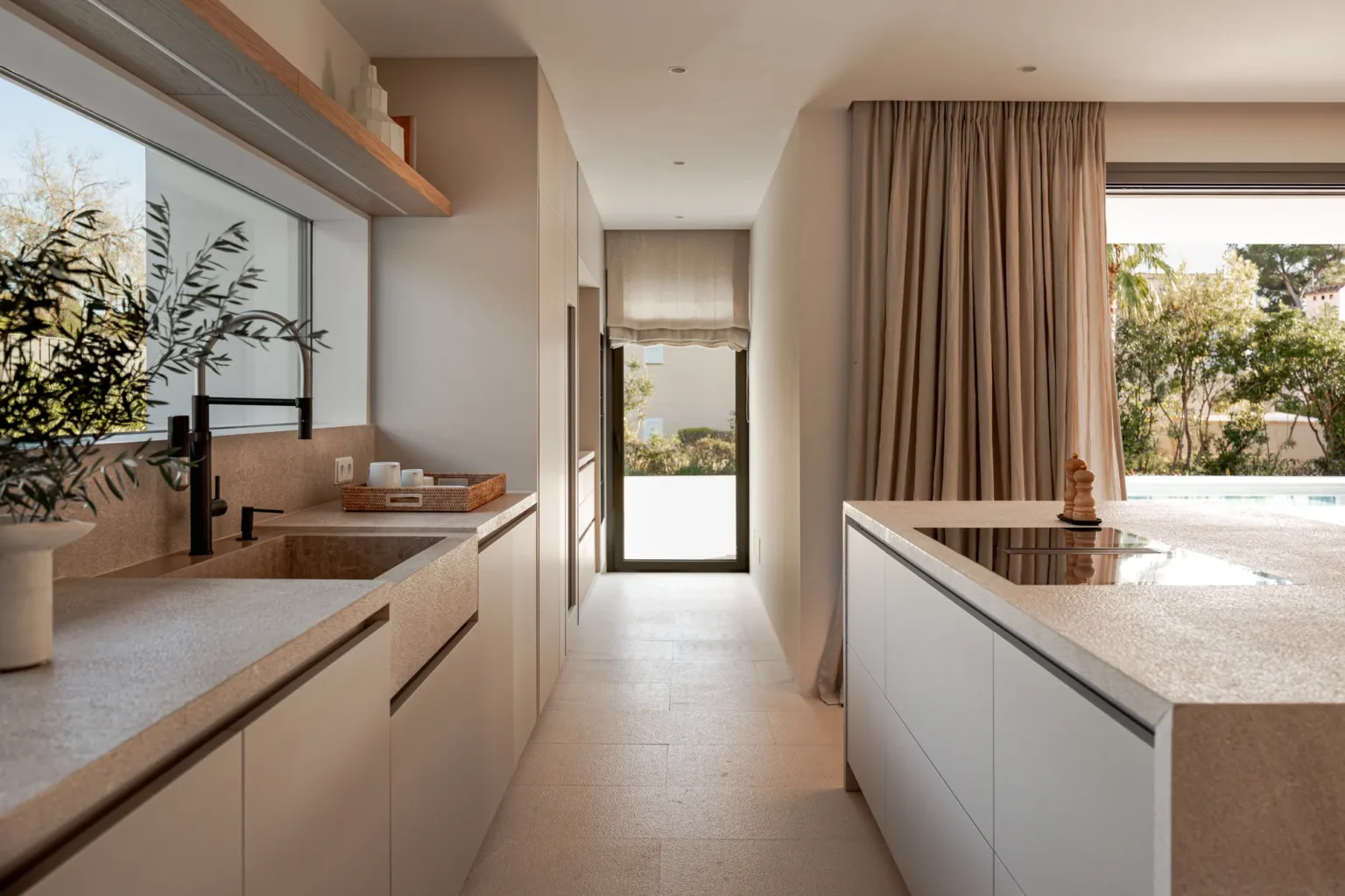 Cocina con isla y vista al pasillo y jardín en el proyecto Pinar de Sa Dutxeta
