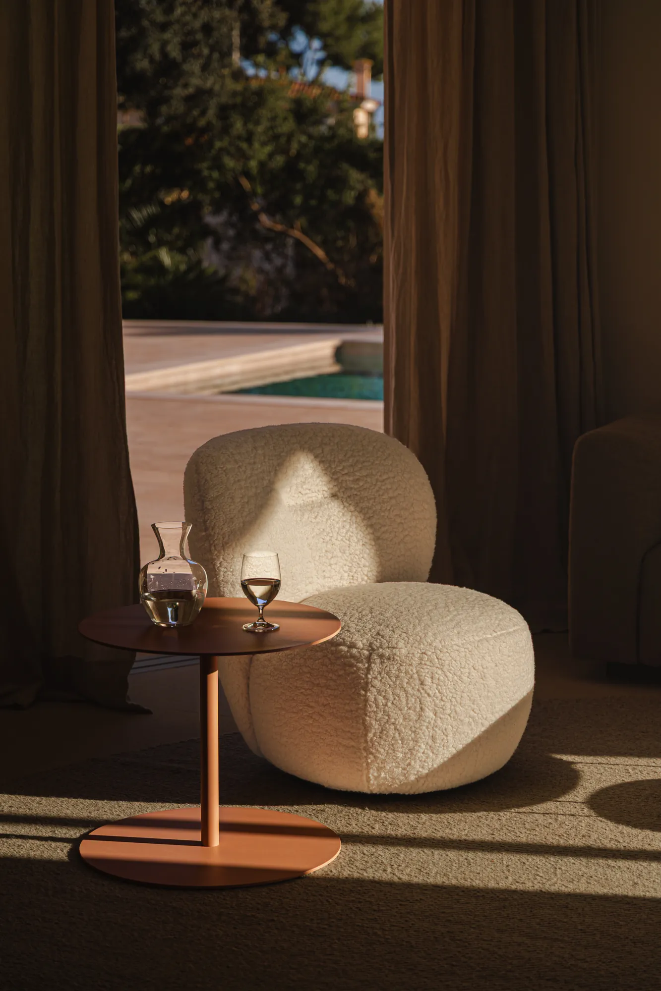 Salón con vista a la piscina y sillón de bouclé en el proyecto Pinar de Sa Dutxeta