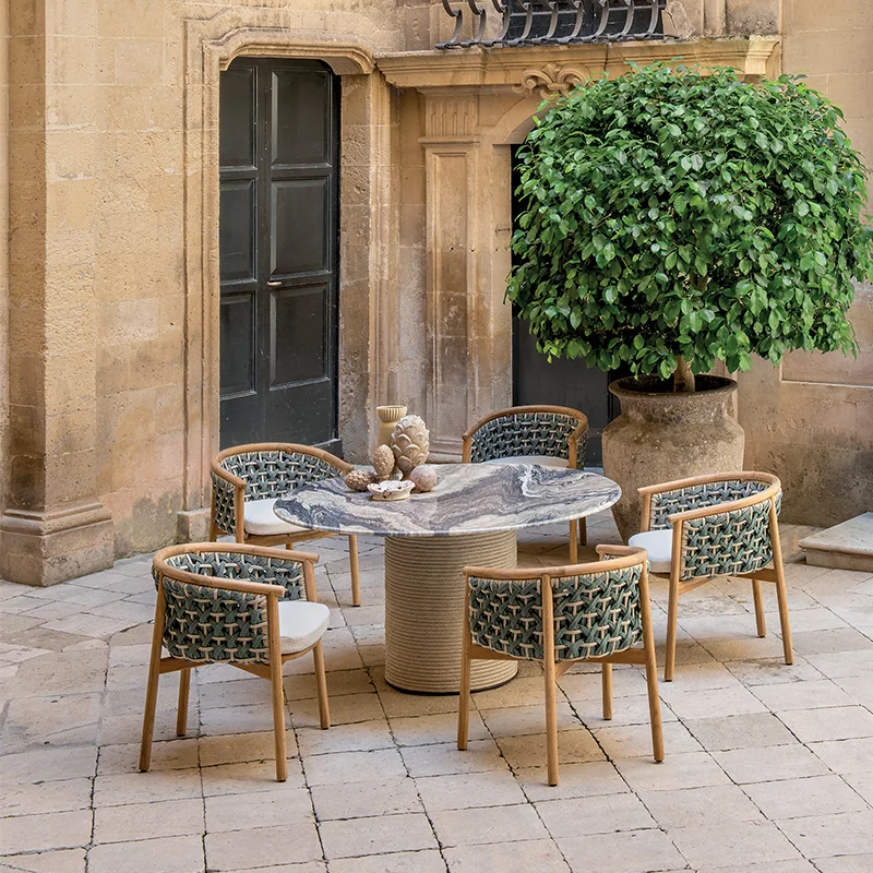 Comedor exterior con mesa redonda y sillas trenzadas de la colección Patio de Ethimo en un patio de piedra