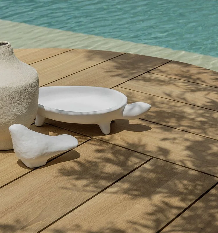 Mesas bajas de exterior sobre tarima de madera junto a la piscina, colección Patio de Ethimo