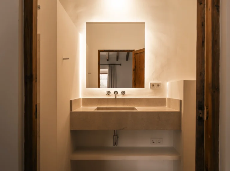 Baño con lavabo de obra y espejo retroiluminado entre marcos de madera en el proyecto 1906 de Sa Dutxeta en Sóller, Mallorca