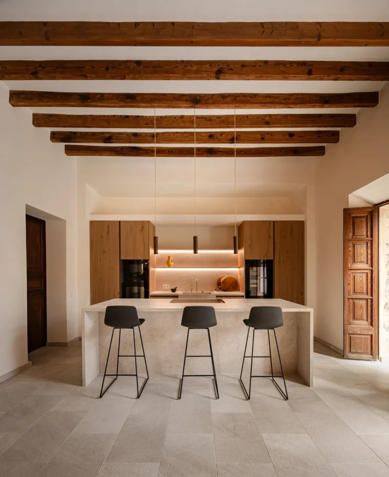 Cocina con isla, vigas de madera originales y puertas antiguas en el proyecto 1906 de Sa Dutxeta en Sóller, Mallorca