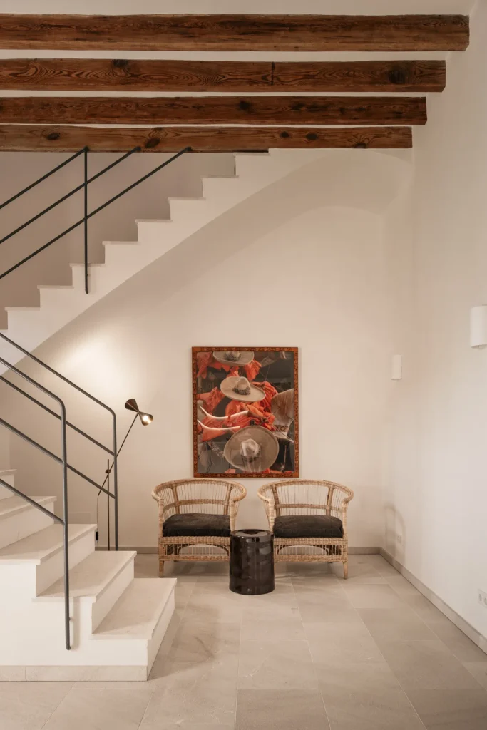 Escalera de obra y rincón de descanso bajo vigas de madera originales en el proyecto 1906 de Sa Dutxeta en Sóller, Mallorca